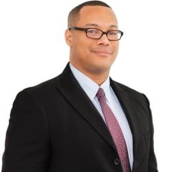 Sterling Brown, Used Car Manager at Hyundai of Moreno Valley, wearing a black suit, light blue shirt, and patterned tie, posing confidently.
